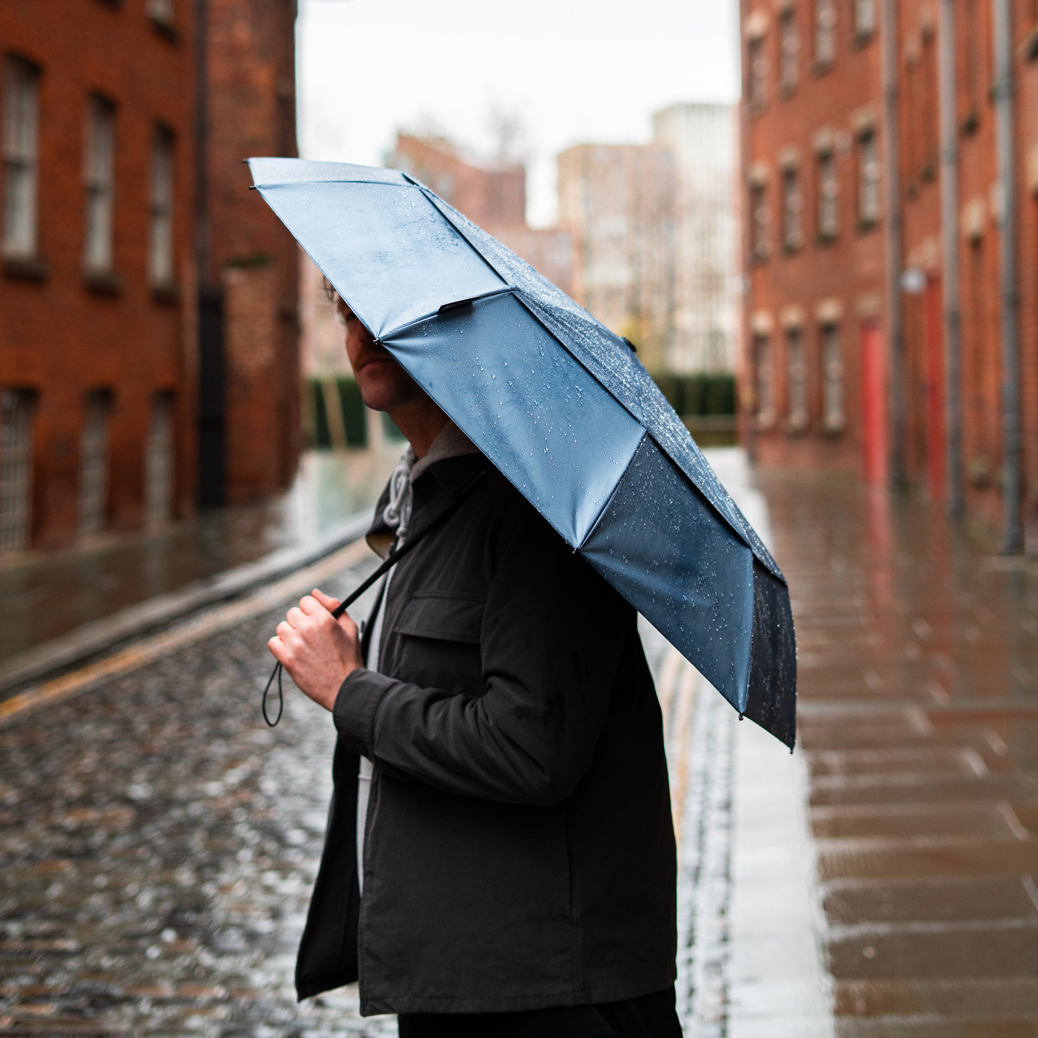 Manchester brolly brand SOAKED showing an Atlantic Mist umbrella on a cobbled rainy street