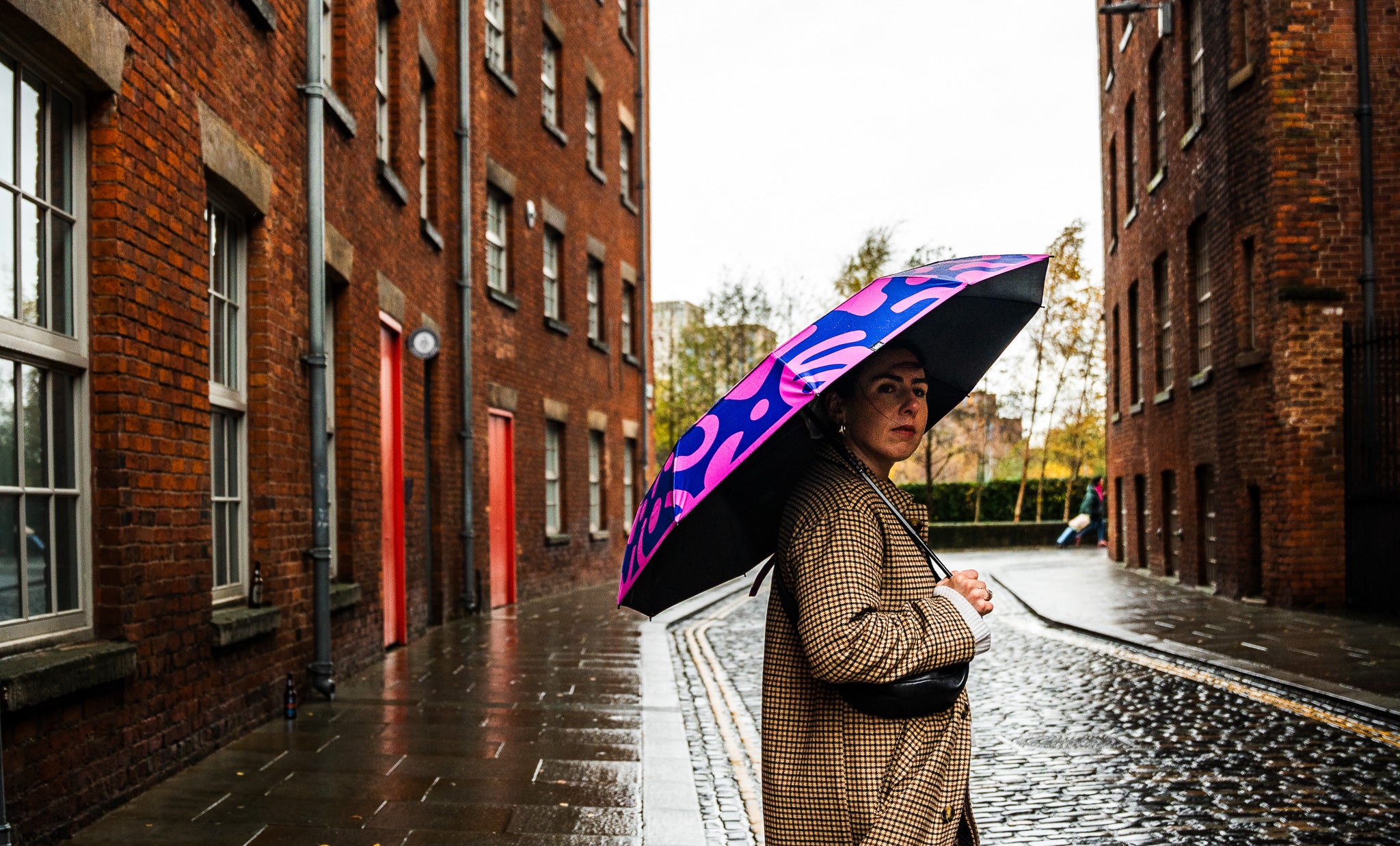 Person holding a colourful sustainable eco-conscious umbrella on a rainy Manchester UK street.