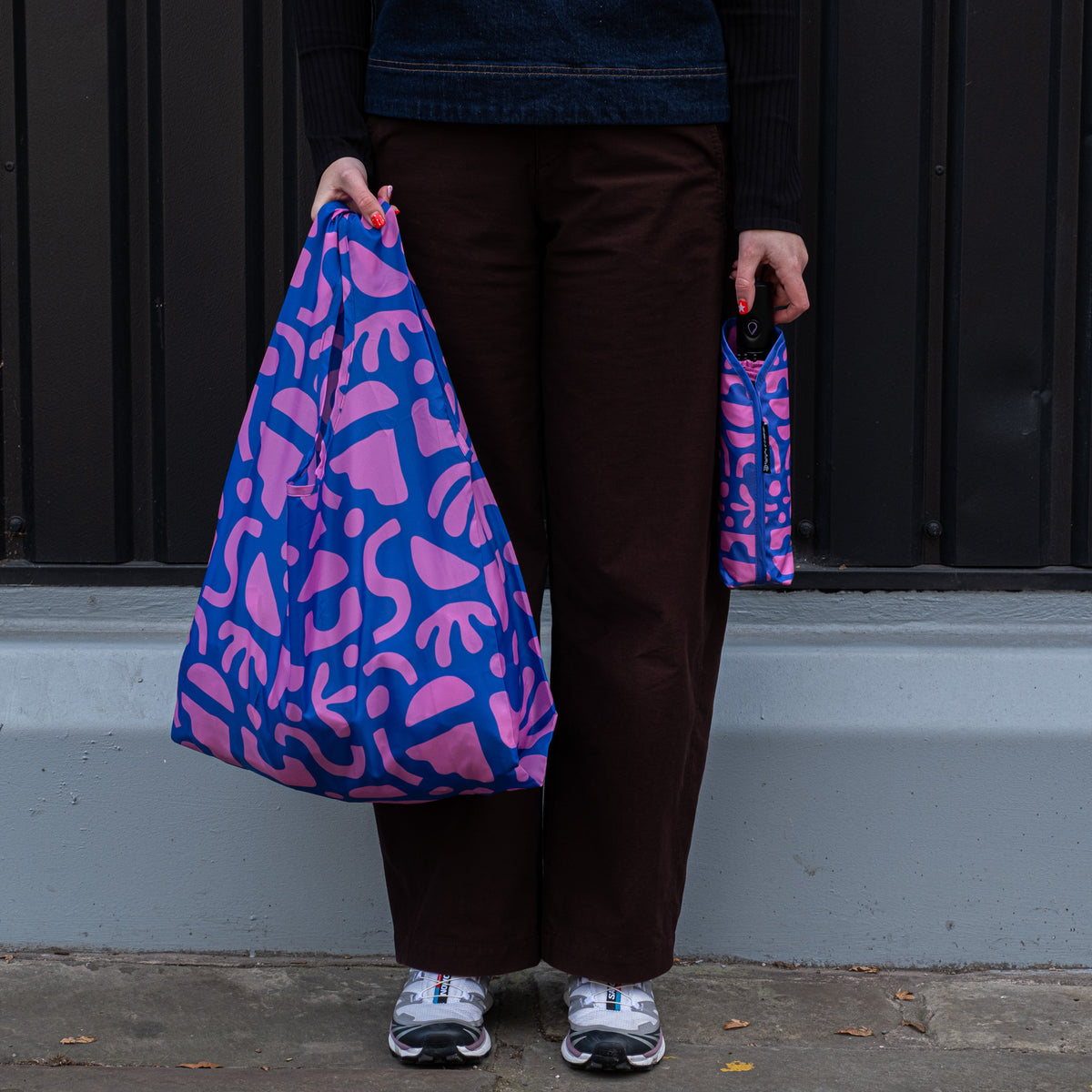 Person standing outside holding the SOAKED Bits and Bobs purple and blue tote bag open and the umbrella in its sleeve