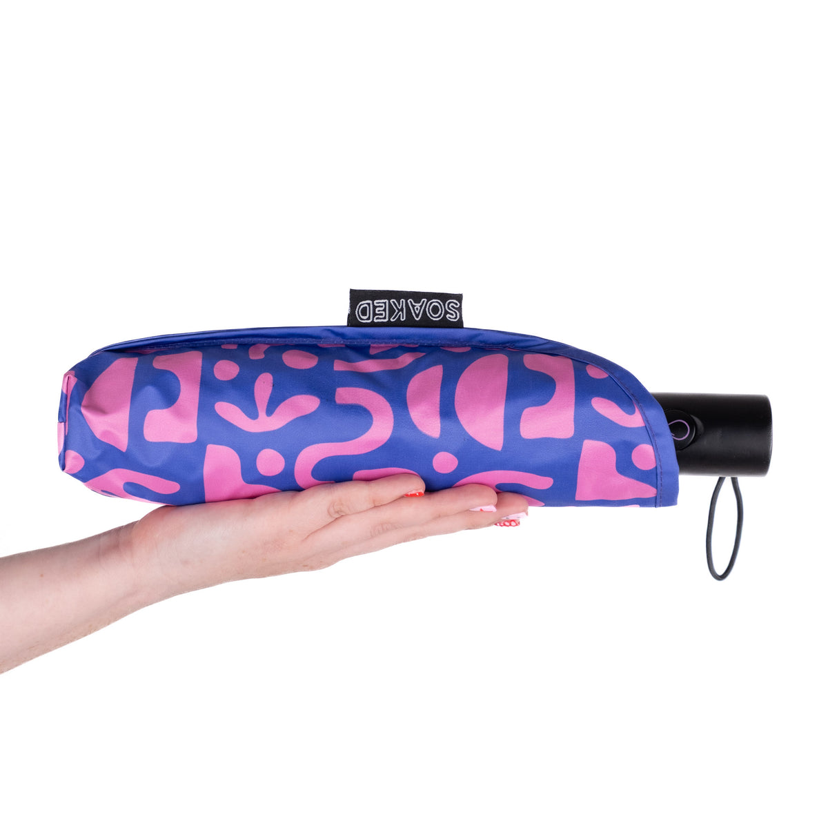 Hand holding the SOAKED Bits and Bobs purple and blue umbrella in its waterproof sleeve made from recycled plastic