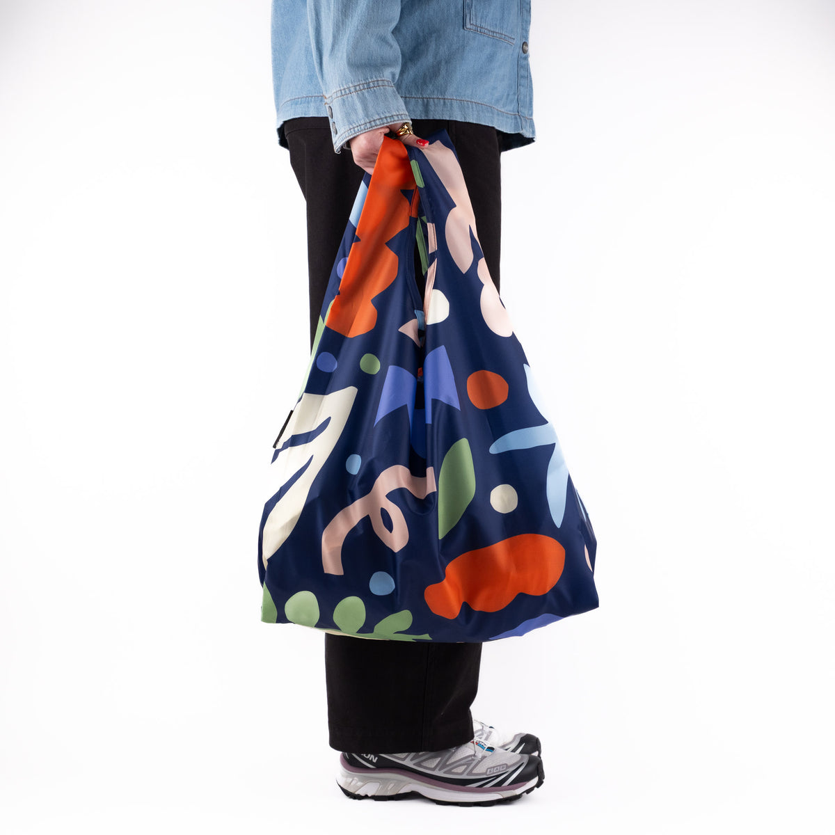 Person standing side-on with the SOAKED Block Party abstract blue and purple tote bag
