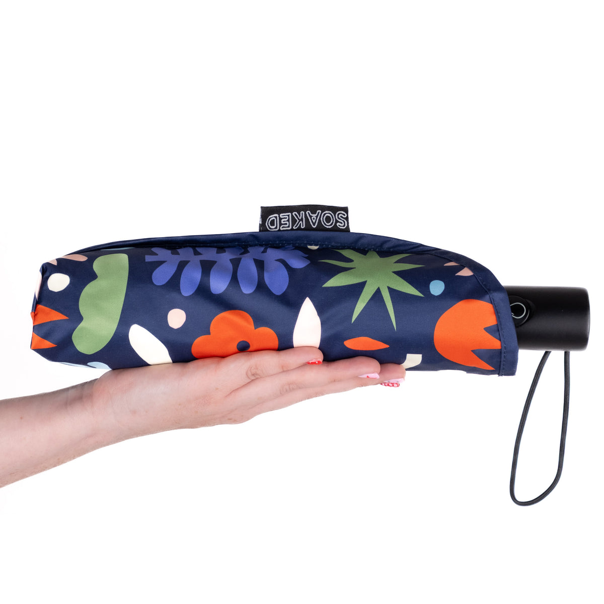 Hand holding the SOAKED Block Party abstract blue and purple umbrella in its waterproof sleeve made from recycled plastic