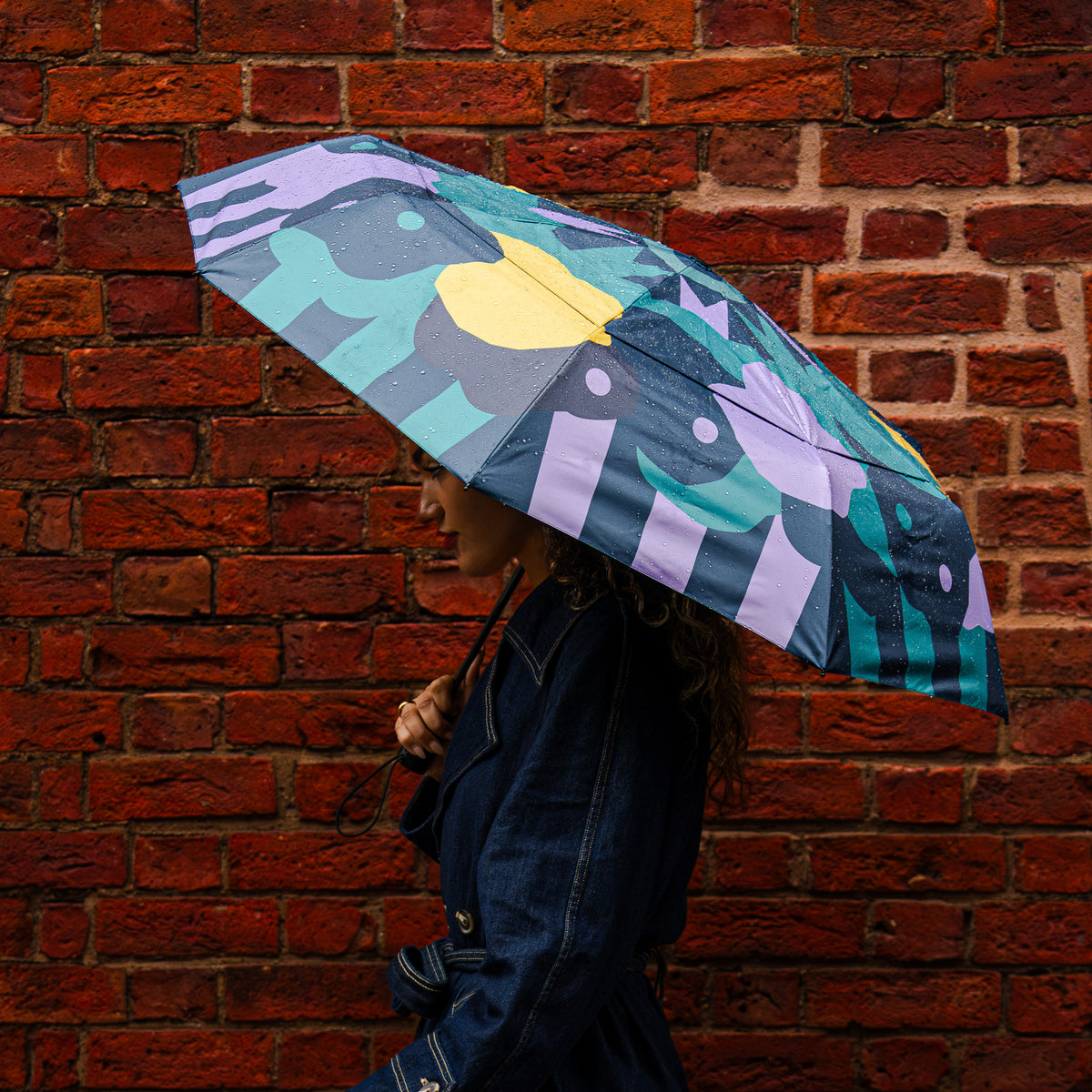 Model holding the SOAKED Cloudburst cloud and floral umbrella in the rain, showing the recycled-bottle canopy