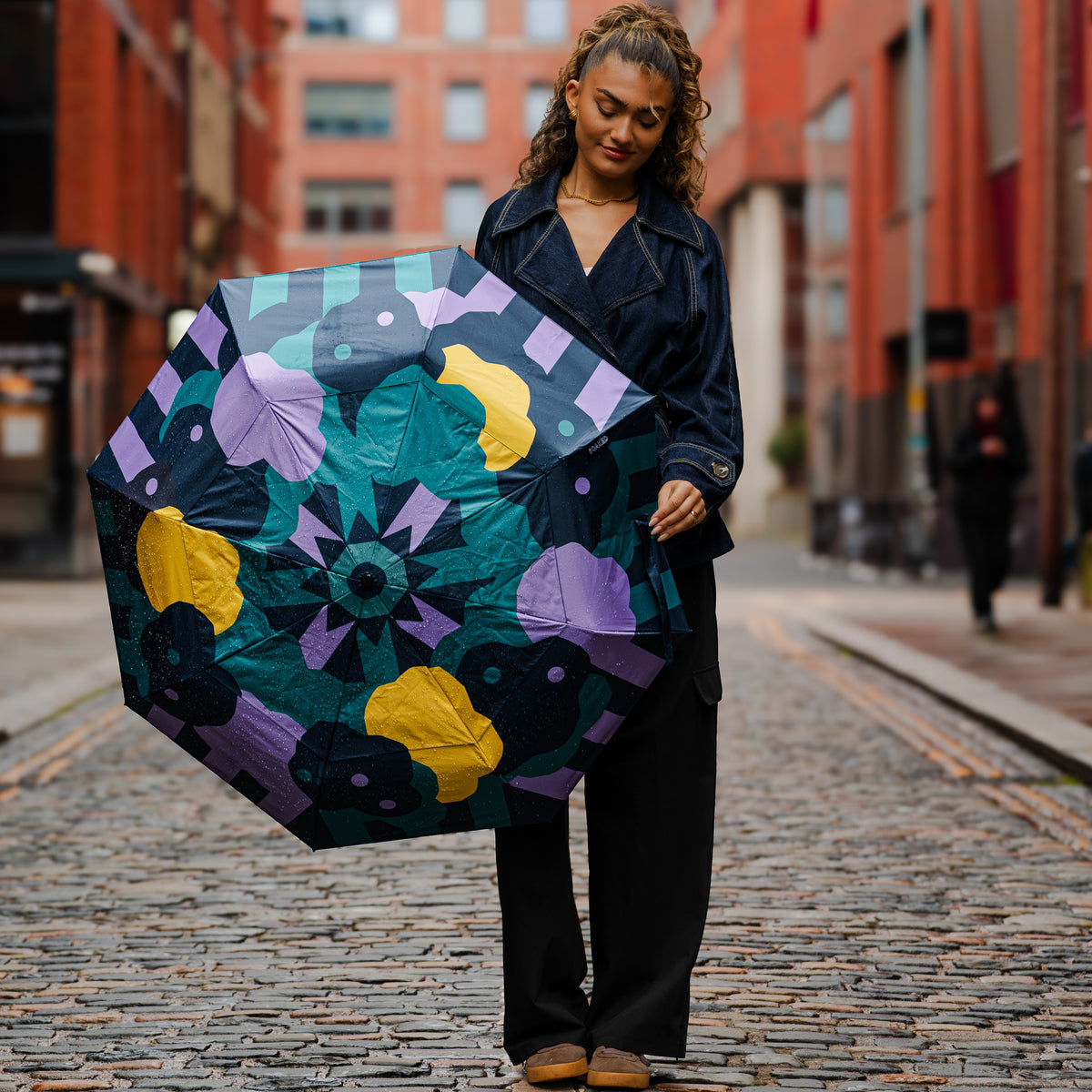 Model walking down a cobbled street carrying the open SOAKED Cloudburst cloud and floral umbrella