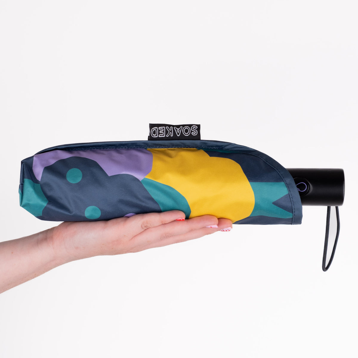 Hand holding the SOAKED Cloudburst cloud and floral umbrella in its waterproof sleeve made from recycled plastic