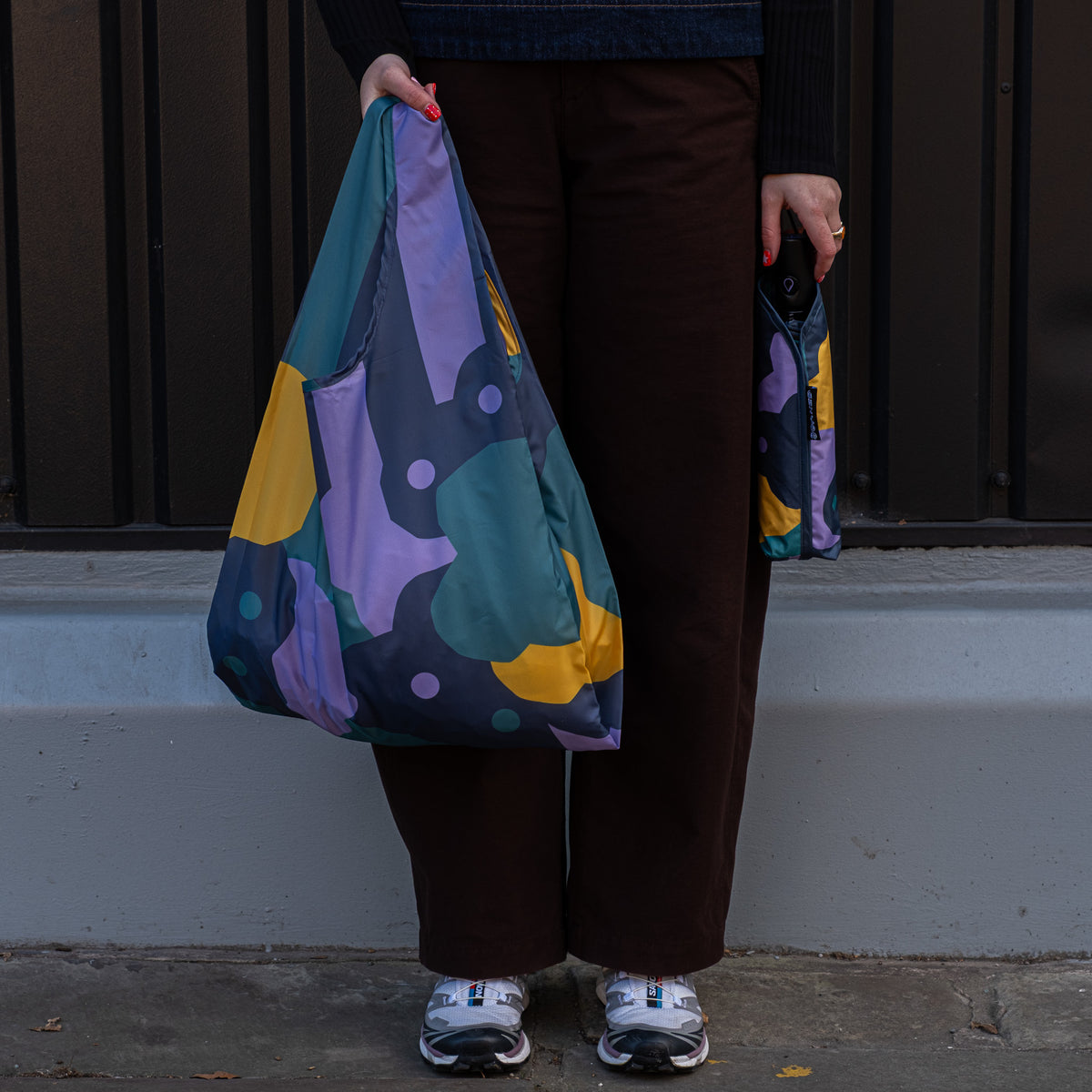 Person standing outside holding the SOAKED Cloudburst cloud and floral tote bag open and the umbrella in its sleeve