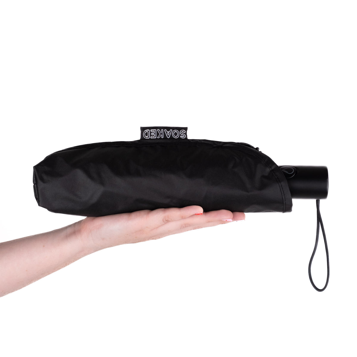 Hand holding the SOAKED Dark Skies black umbrella in its waterproof sleeve made from plastic