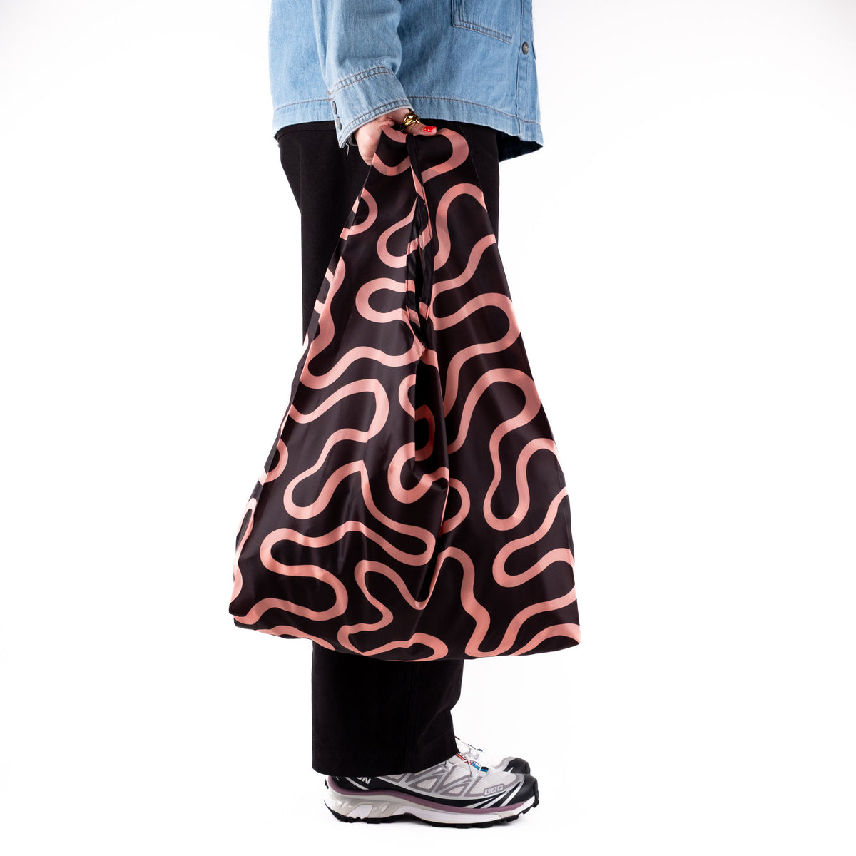 Person standing side-on with the SOAKED Doodle black and peach swirl tote bag