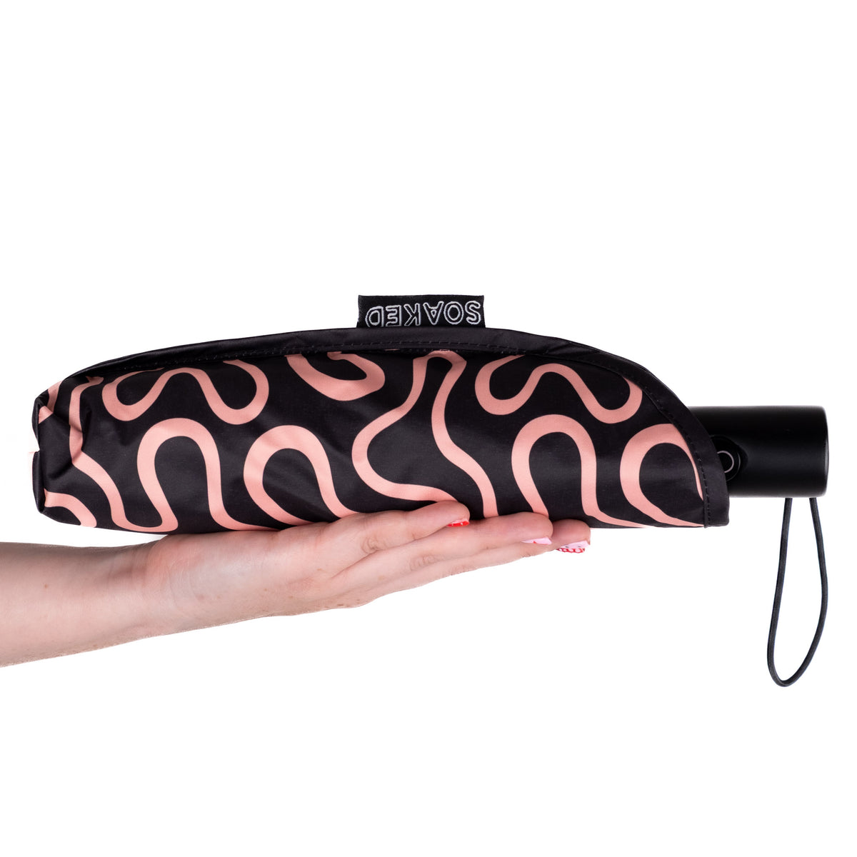 Hand holding the SOAKED Doodle black and peach swirl umbrella in its waterproof sleeve made from plastic