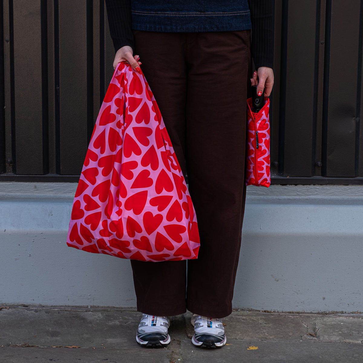Person standing outside holding the SOAKED Love Bug heart print tote bag open and the umbrella in its sleeve