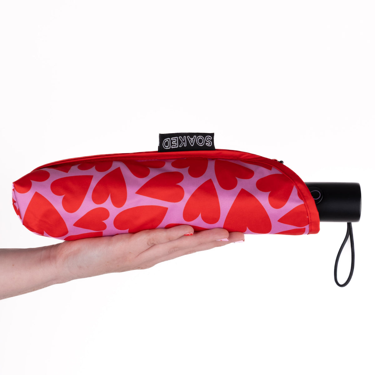 Hand holding the SOAKED Love Bug heart print umbrella in its waterproof sleeve made from recycled plastic