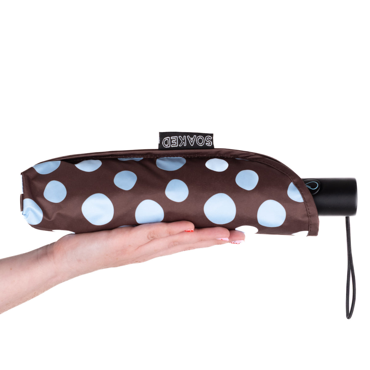 Hand holding the SOAKED Polka brown and sky blue polka dot umbrella in its waterproof sleeve made from recycled plastic