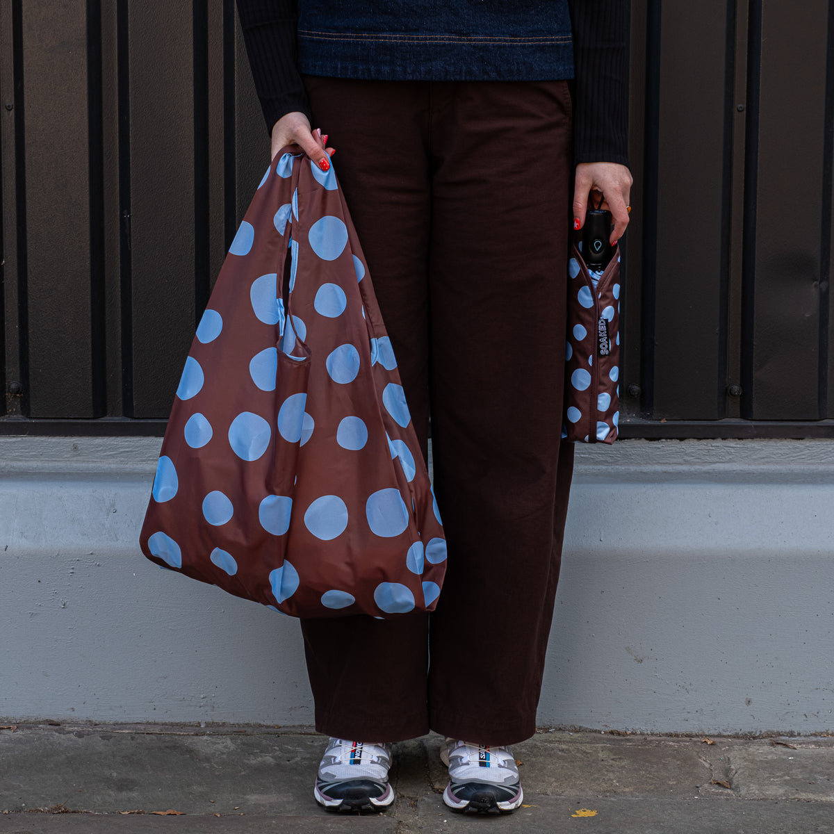 Person standing outside holding the SOAKED Polka brown and sky blue polka dot tote bag open and the umbrella in its sleeve