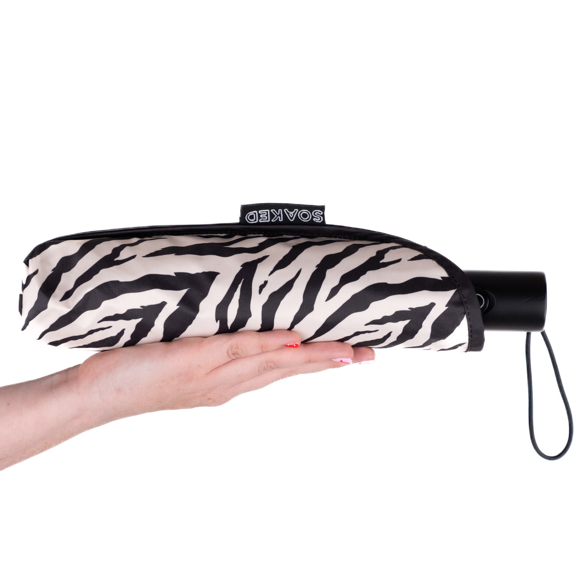 Hand holding the SOAKED Safari zebra print umbrella in its waterproof sleeve made from recycled plastic