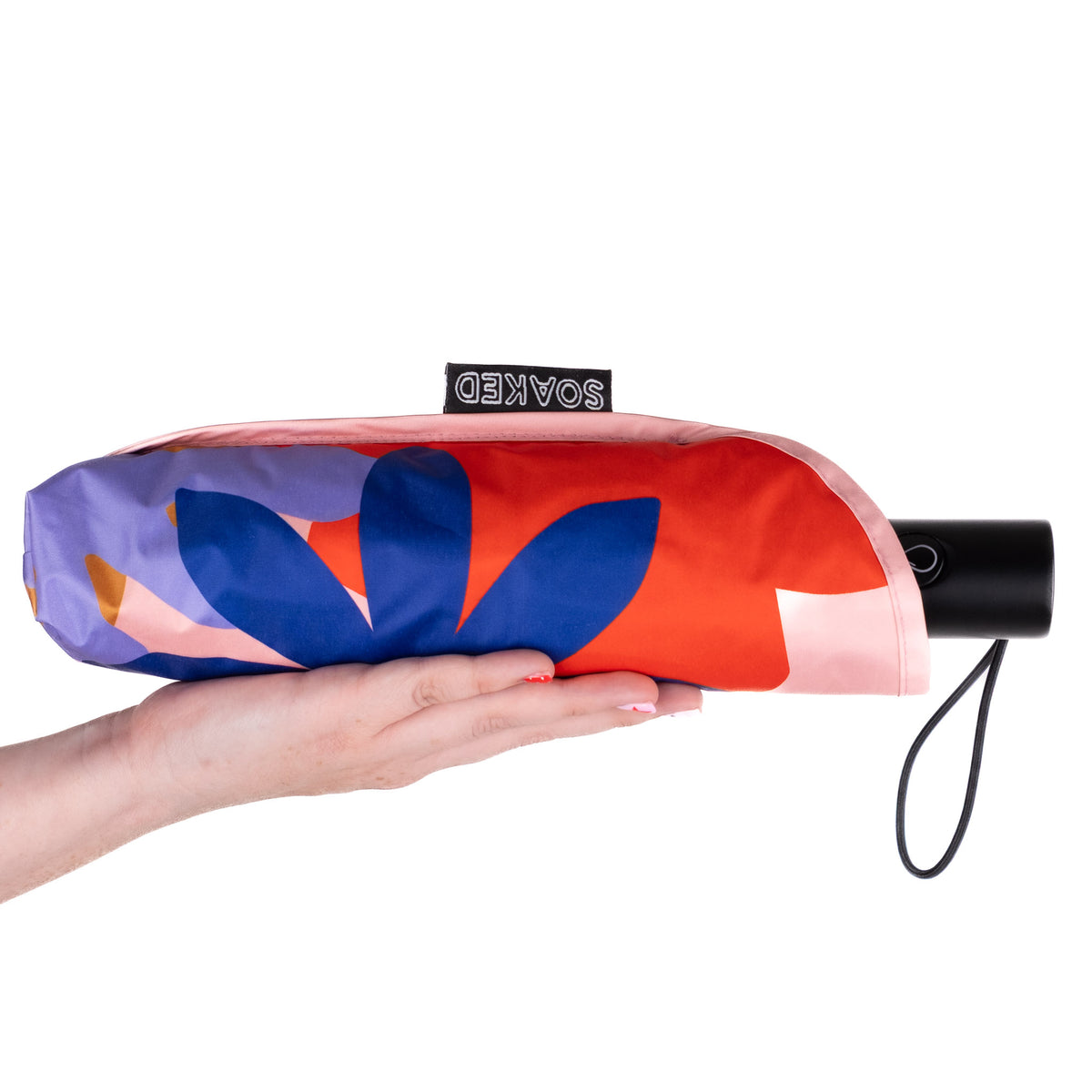 Hand holding the SOAKED Superbloom bold floral umbrella in its waterproof sleeve made from recycled plastic