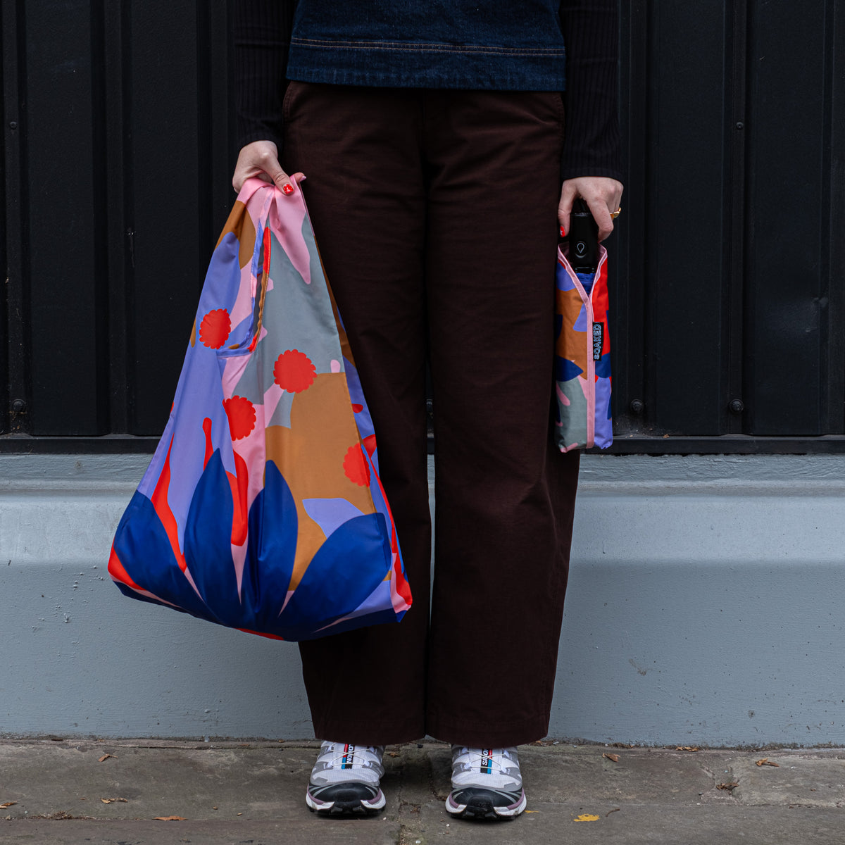 Person standing outside holding the SOAKED Superbloom bold floral tote bag open and the umbrella in its sleeve