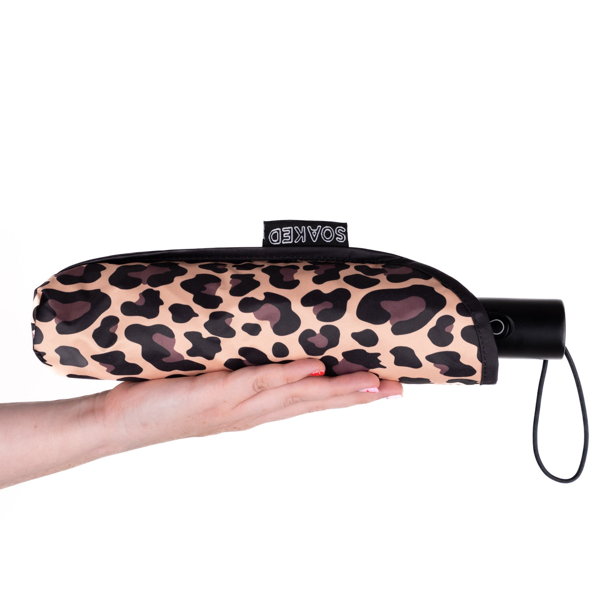 Hand holding the SOAKED Wild Thing leopard print umbrella in its waterproof sleeve made from recycled plastic