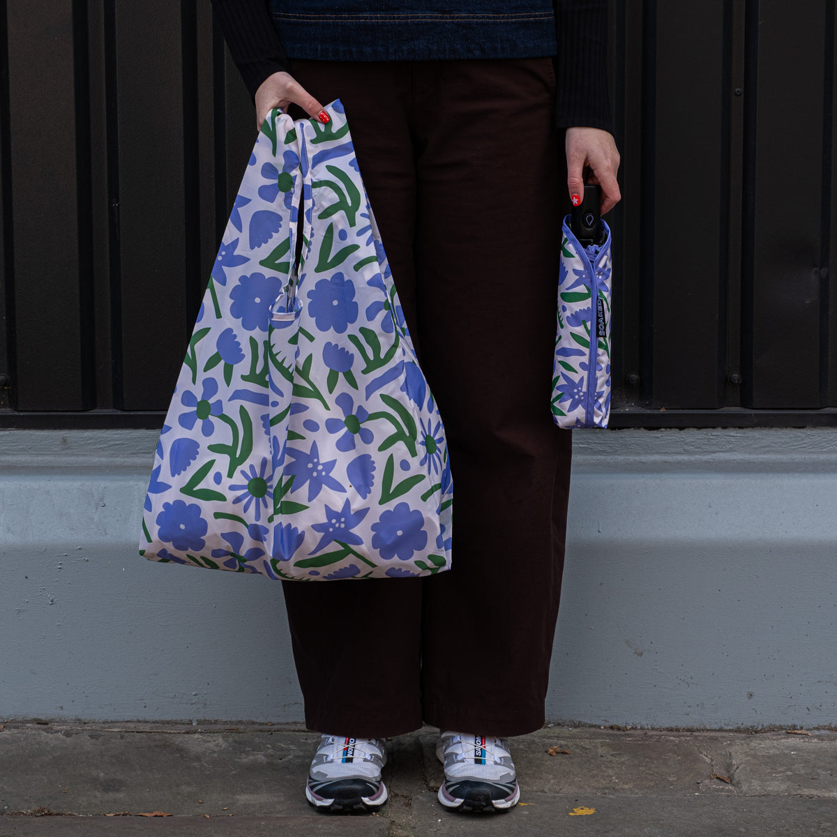 Person standing outside holding the SOAKED Wildflowers floral tote bag open and the umbrella in its sleeve