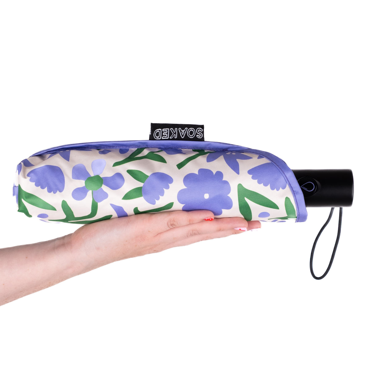 Hand holding the SOAKED Wildflowers floral umbrella in its waterproof sleeve made from recycled plastic